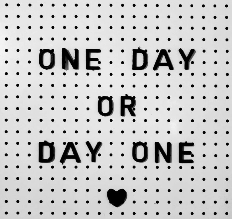 Black letters on white board saying 'One Day or Day One?' with polka dot design.